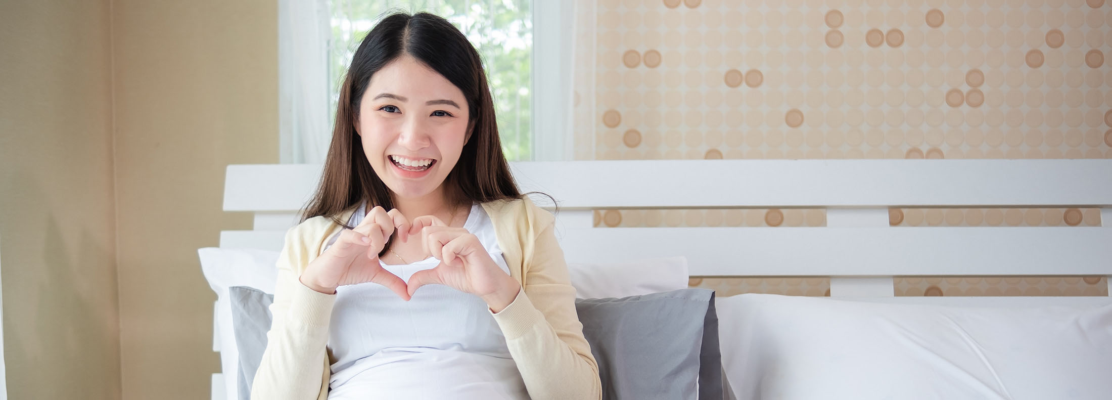 Beautiful woman Asia Happy Is pregnant in bed at home people and expectation concept Female pregnancy Hands holding belly Headphones for children Gray dress teens Will be a mother baby